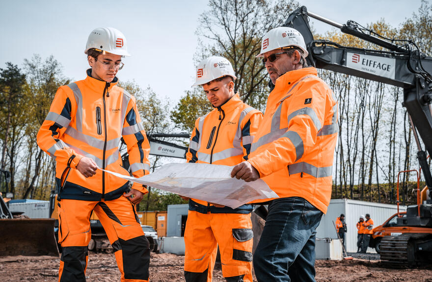 Azibis und der Ausbilder besprechen einen Plan auf der Baustelle.